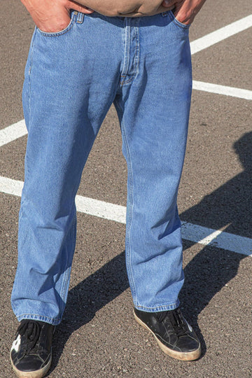 Person wearing blue jeans standing on a paved surface with white lines.