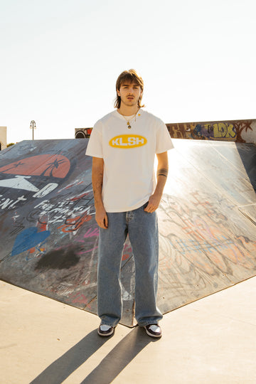 Person wearing a white t-shirt with a faded denim jeans at a skate park