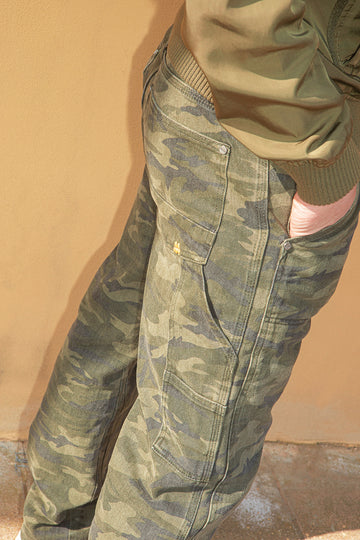 Camouflage pants worn by a person against a beige wall.