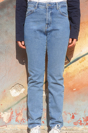 Person wearing faded blue slim-fit jeans standing against a textured wall.
