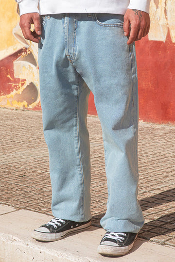 Person wearing light blue jeans and a white sweatshirt standing against a colorful wall.
