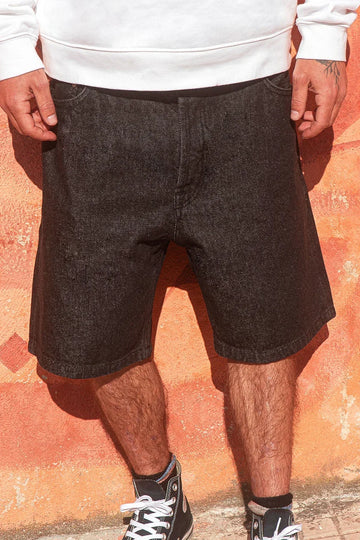 Person wearing dark denim shorts with a white sweatshirt against an orange wall.