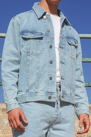 Person wearing a light blue denim jacket and jeans standing against a graffiti-covered wall.