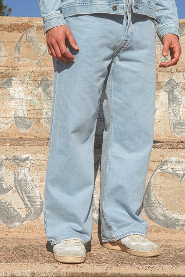 Light Y2K trend blue jeans worn by a person against a textured wall.