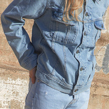 Person wearing a denim outfit standing against a textured wall.