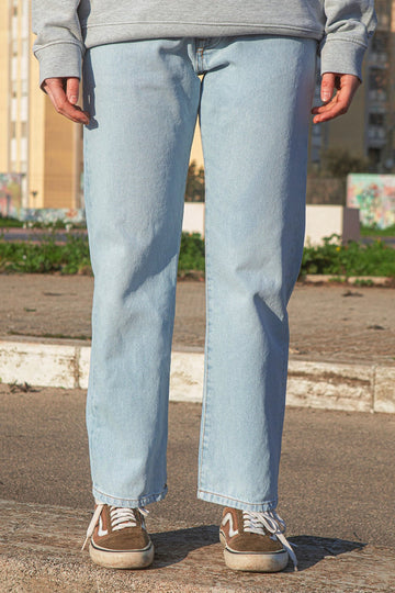 Person wearing light blue jeans and a gray sweatshirt standing on a street.