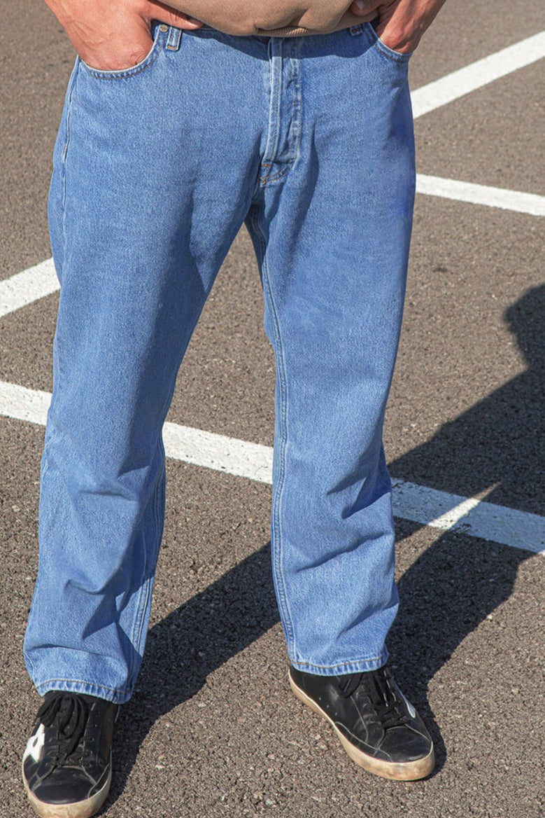 Person wearing blue jeans standing on a paved surface with white lines.