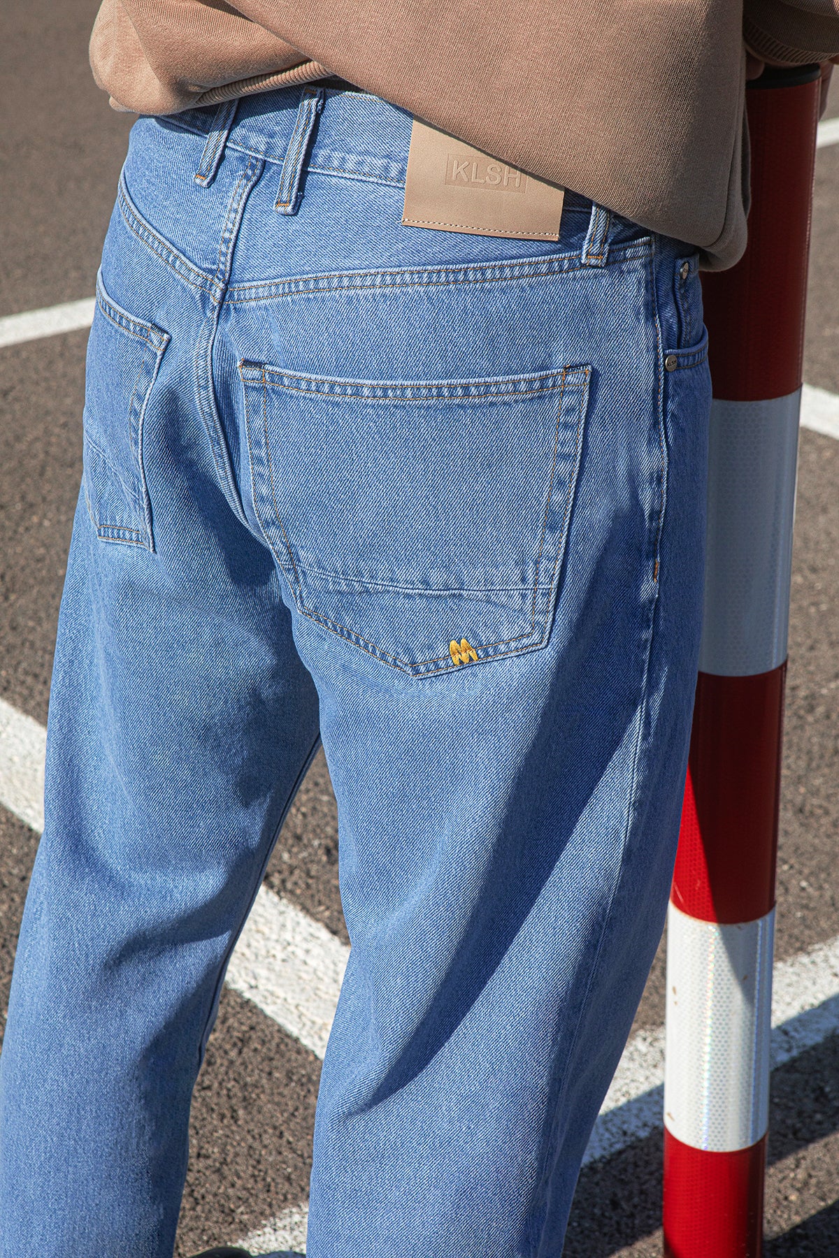 Person wearing blue jeans with a brand logo, standing next to a red and white striped pole.