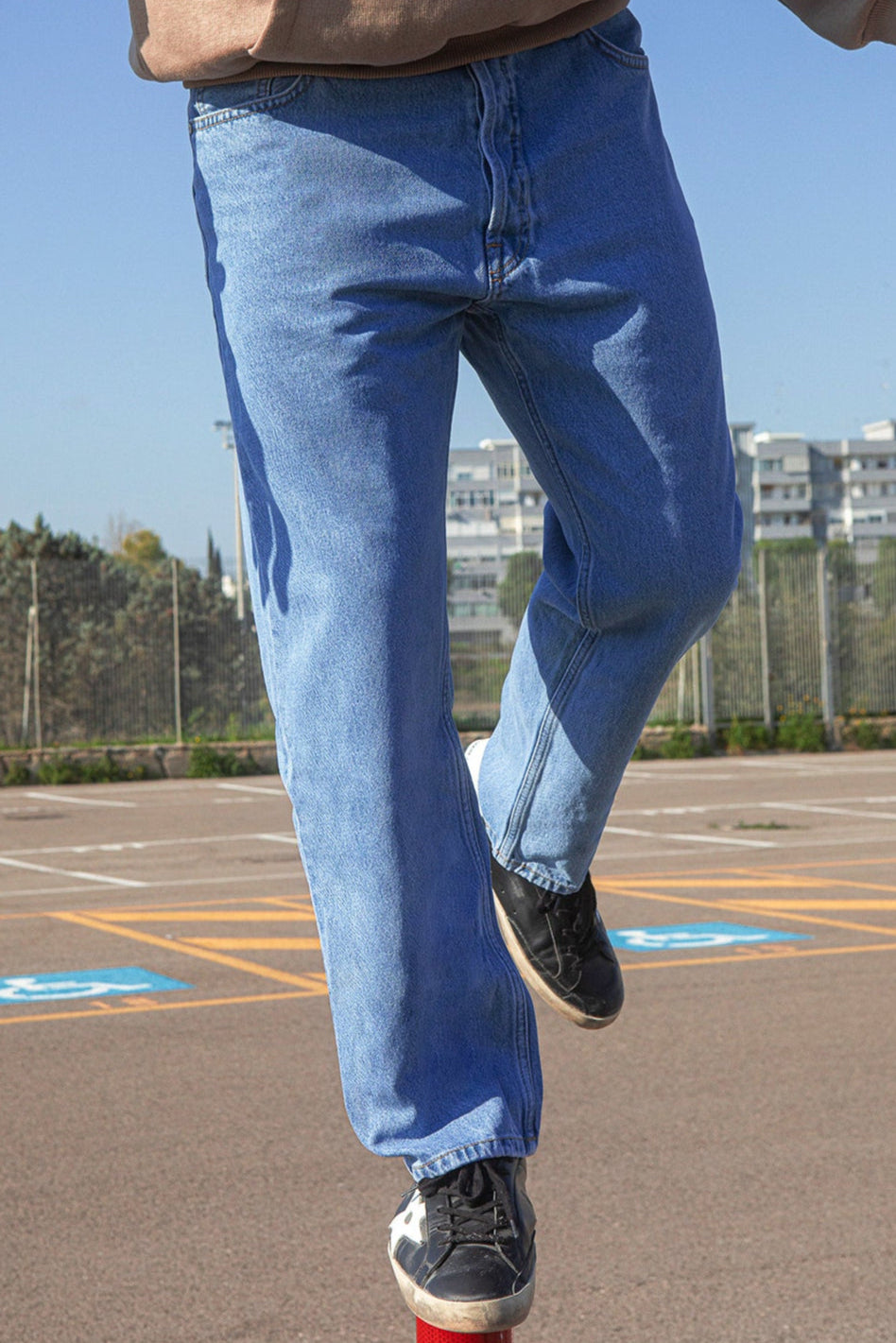 Person wearing blue jeans standing on a paved surface with white lines.