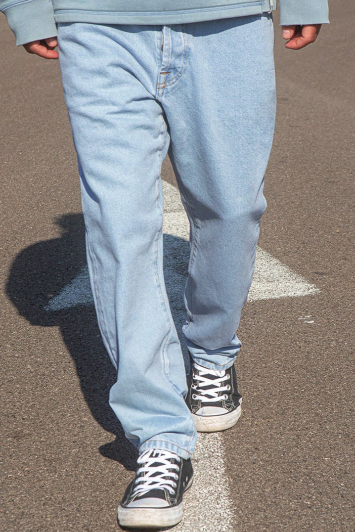 Person wearing BENJI oversized clear sky jeans and black sneakers on a pavement.