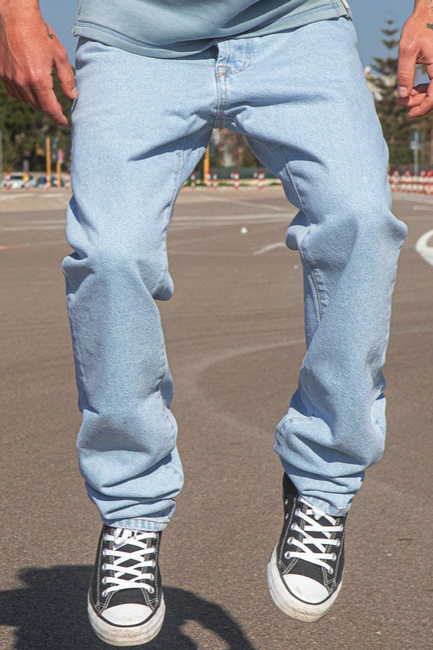 Person wearing BENJI oversized clear sky jeans and black sneakers on a pavement.