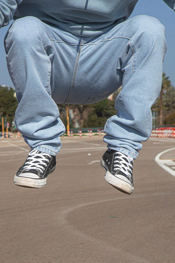 Person wearing  BENJI oversized cler sky italian denim and black sneakers jumping on a basketball court.