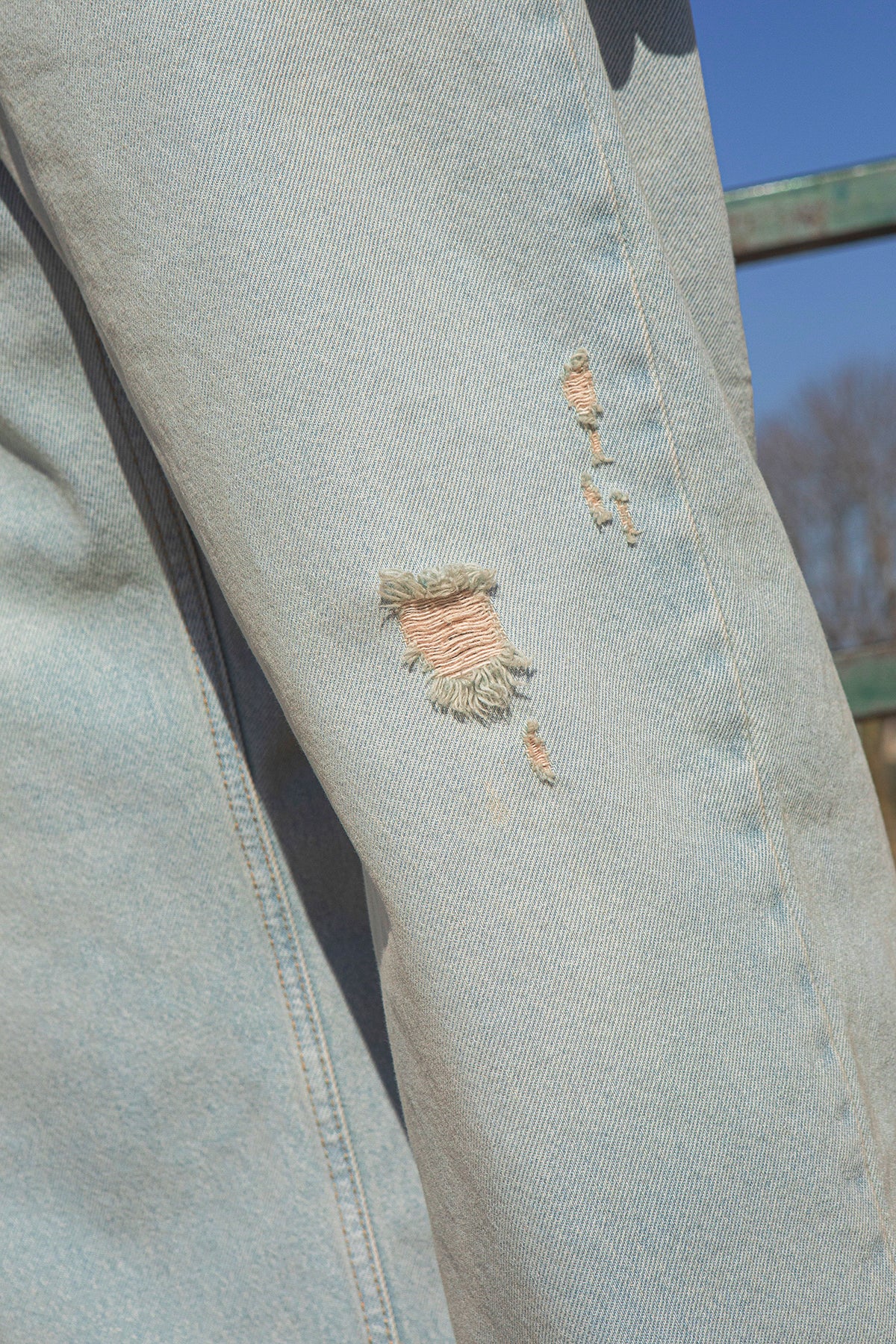 Light blue denim jacket with a small tear on the sleeve against a blurred outdoor background