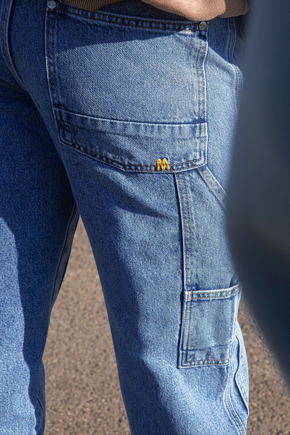 Close-up of blue jeans with KLSH logo on the pocket.