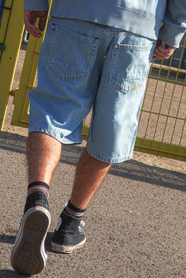 Person wearing light blue denim shorts and black Converse shoes on a street.