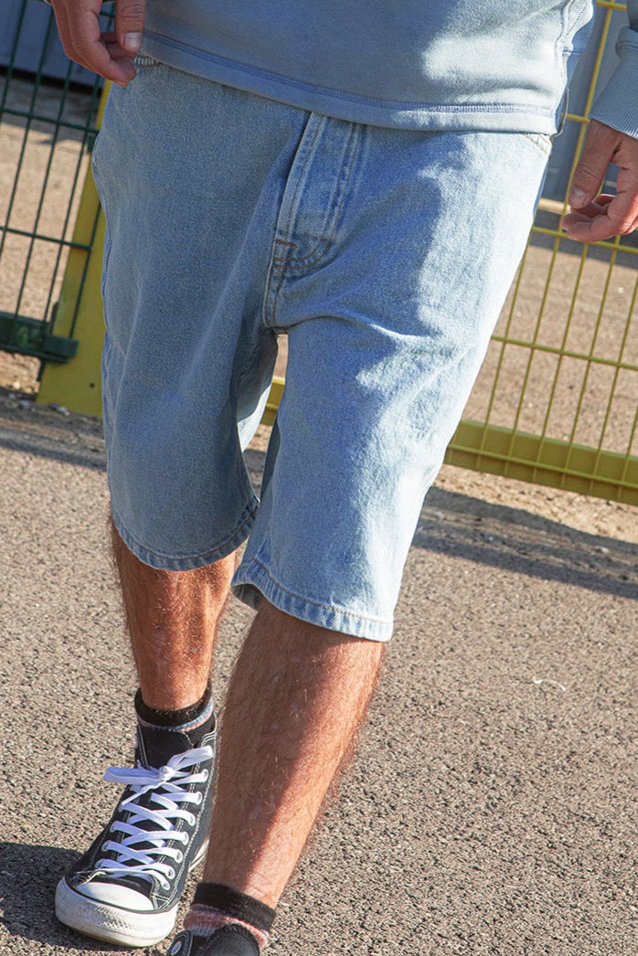 Person wearing light blue denim shorts and black Converse shoes on a street.