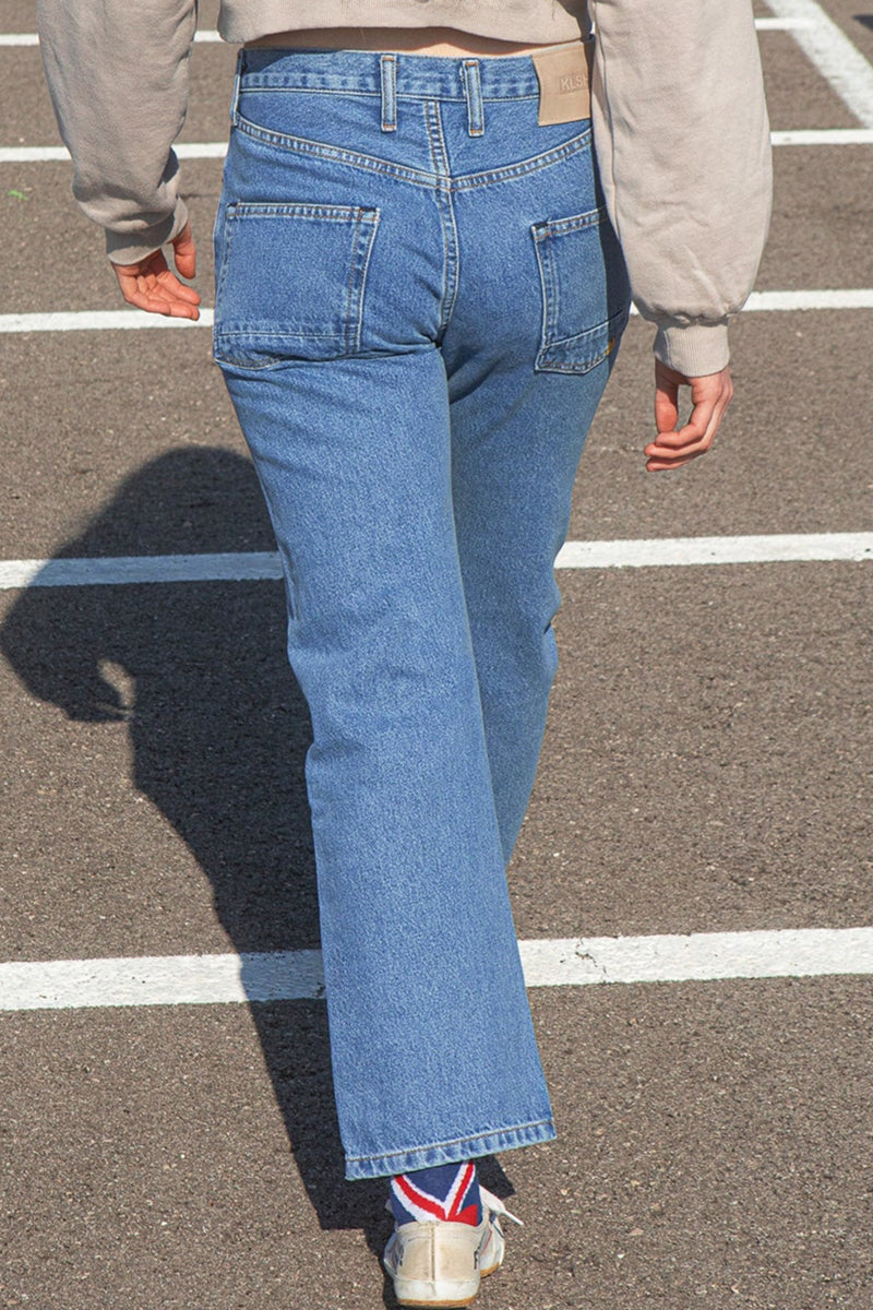 Person wearing the KLSH  RYAN faded blue jeans walking on a road with a neutral background