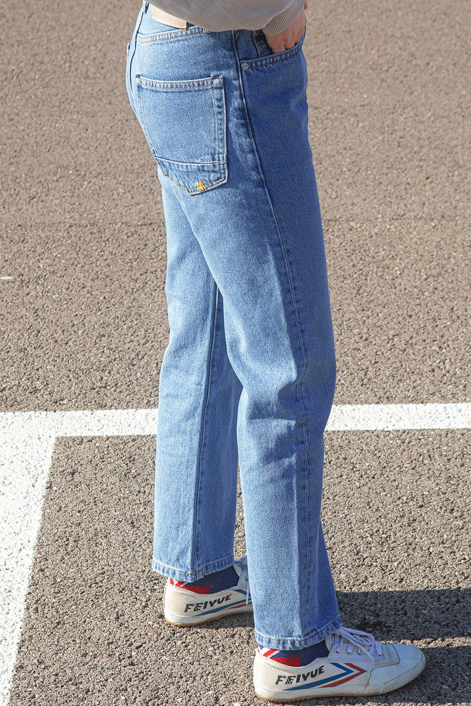 Person wearing the KLSH RYAN faded blue jeans and white sneakers on a concrete surface
