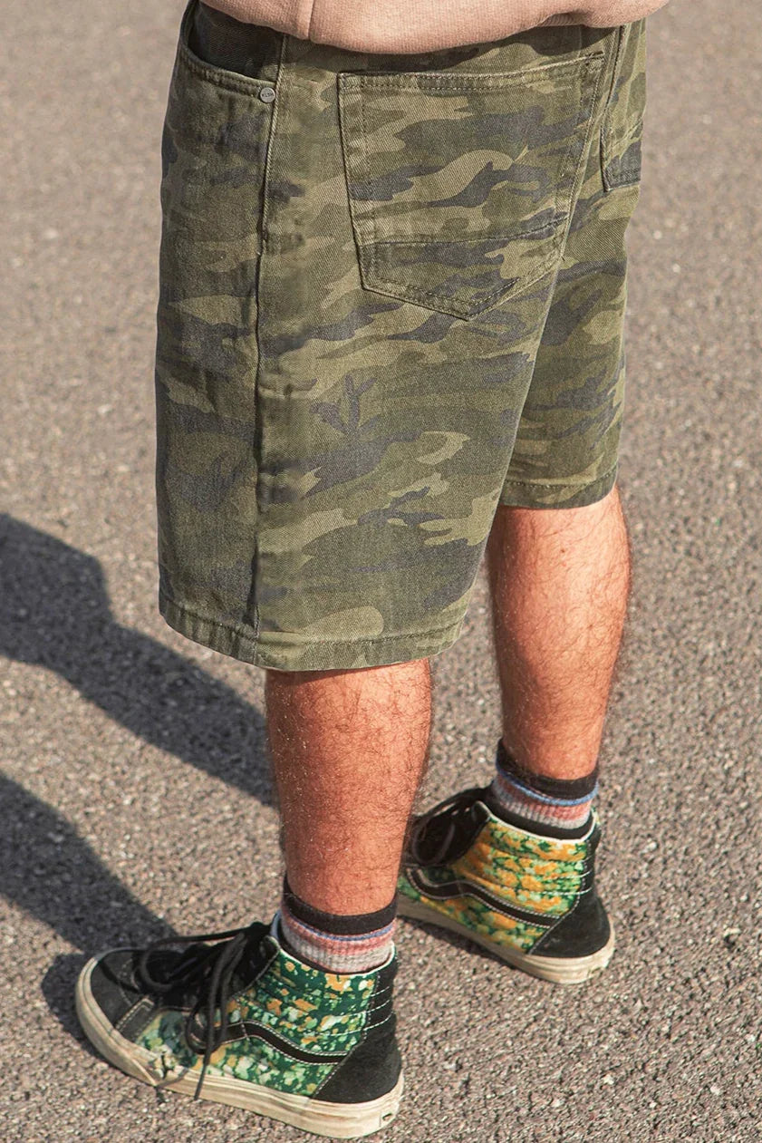 Person wearing camouflage shorts and colorful sneakers on a concrete surface