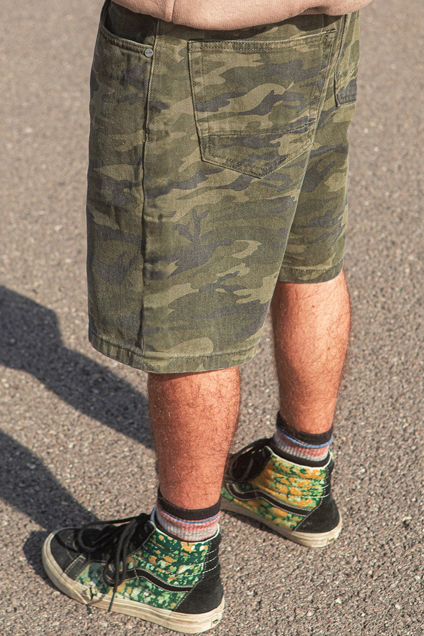 Person wearing camouflage shorts and colorful sneakers on a concrete surface