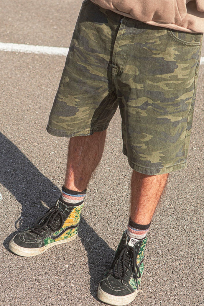 Person wearing camouflage shorts and sneakers with a red object in the background