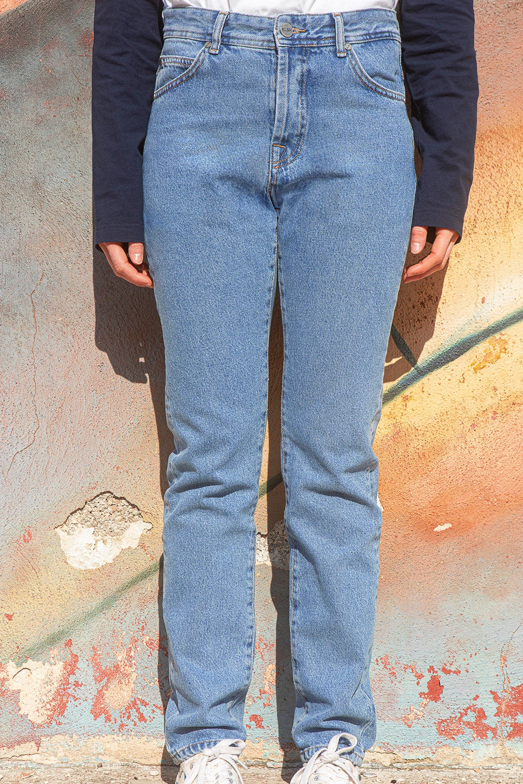Person wearing  faded blue slim-fit jeans standing against a textured wall.