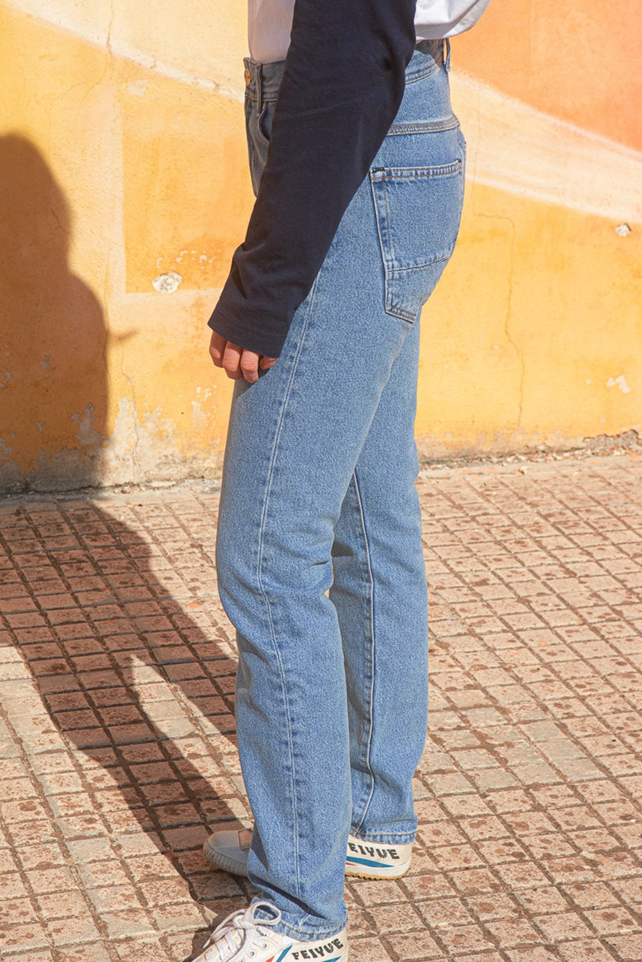Person wearing  faded blue slim-fit jeans standing against a textured wall.