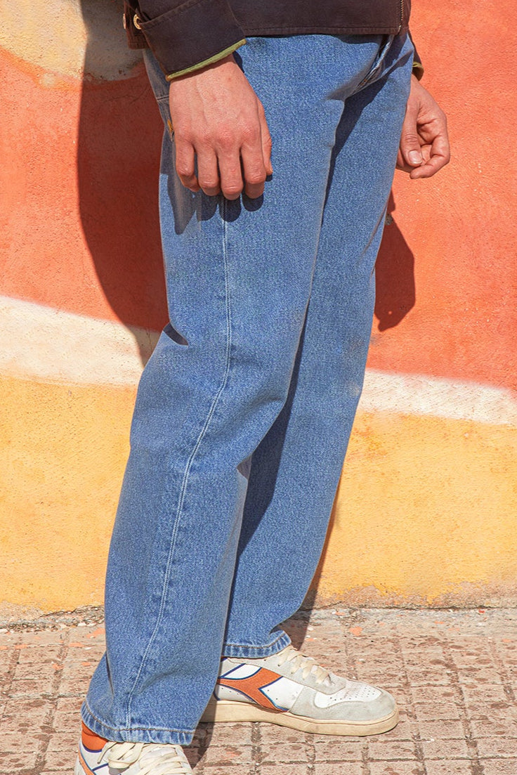 Person wearing blue jeans and white sneakers against a colorful wall.