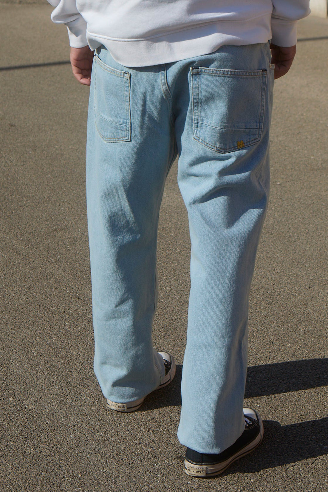 Person wearing light blue jeans and a white sweatshirt standing against a colorful wall.