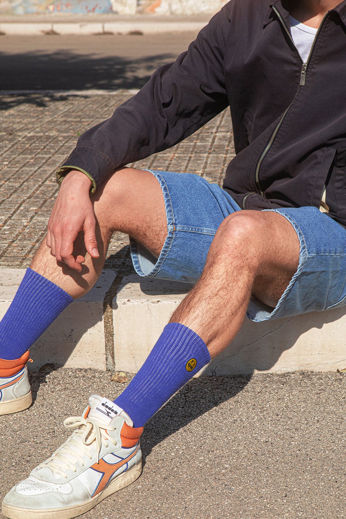 Person wearing blue socks with orange accents and white sneakers sitting on a curb.