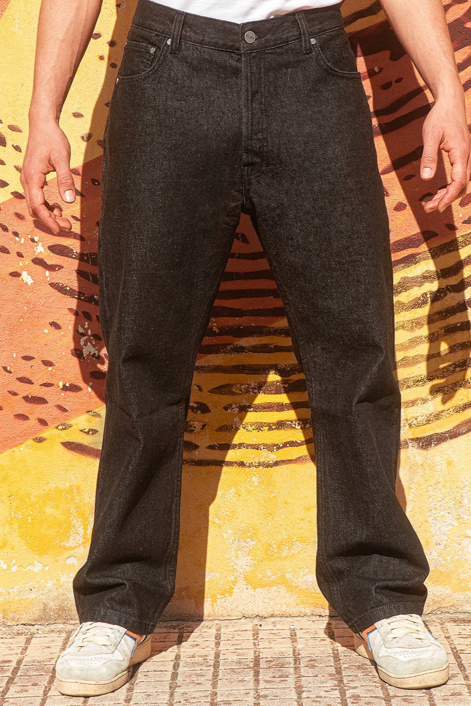 Person wearing BENJI oversized black jeans and a white shirt against a colorful wall.