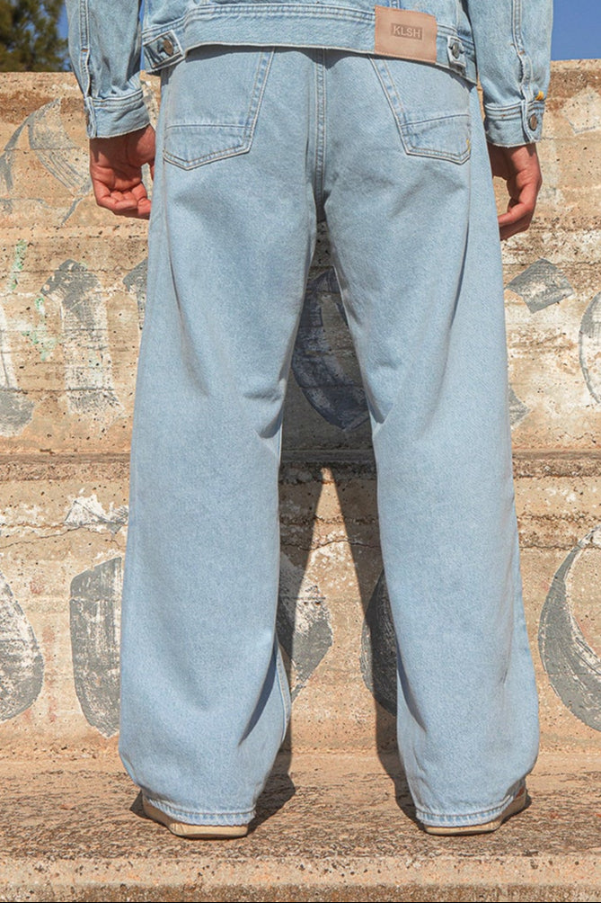 Person wearing a light blue denim  (wide flare style) outfit standing on wooden steps with a clear blue sky.