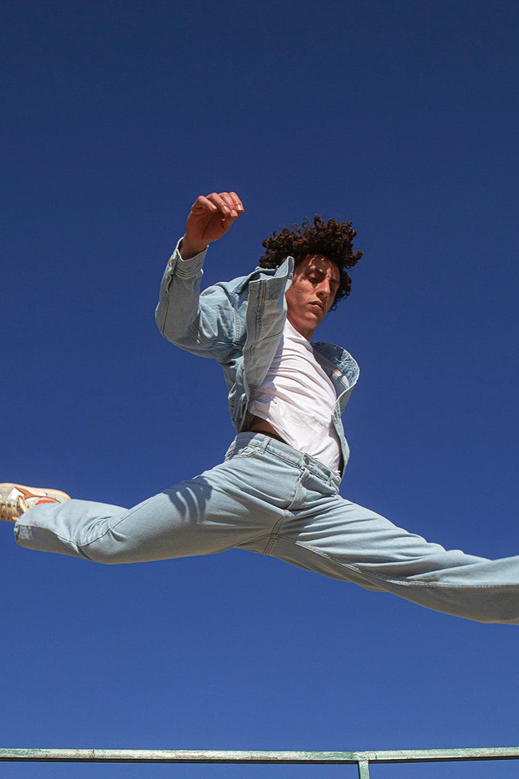 Person in light blue outfit jumping against a clear blue sky