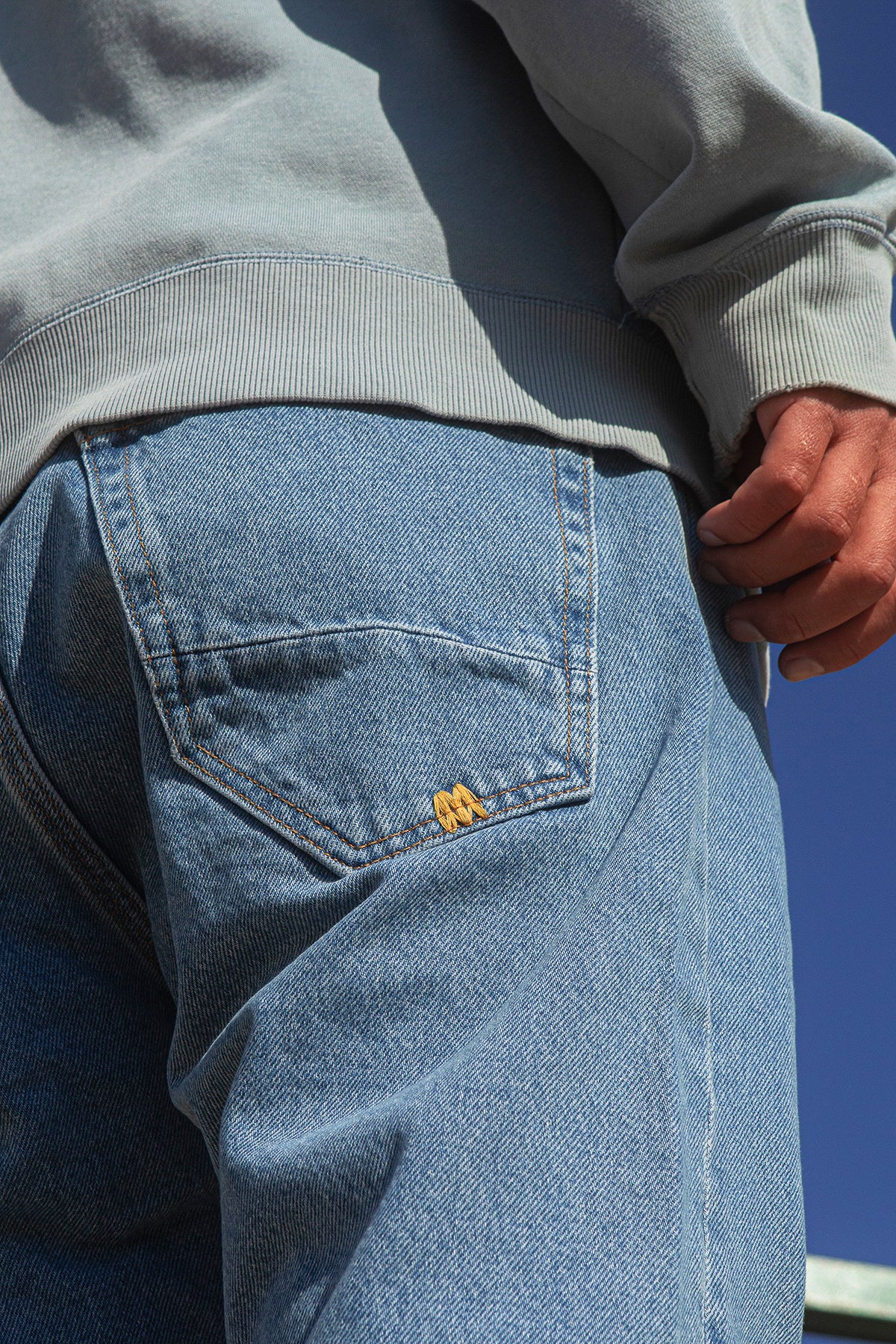 Close-up of faded blue jeans with a brand logo against a clear blue sky