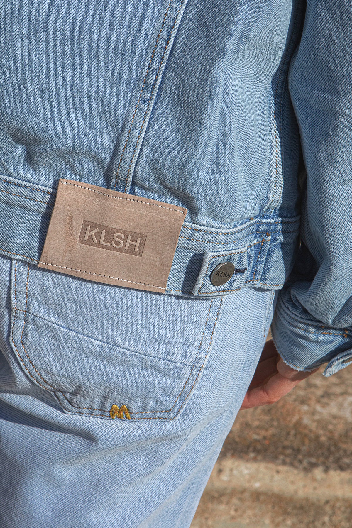 Light blue denim jacket with a brown patch labeled 'KLSH' on a blurred background