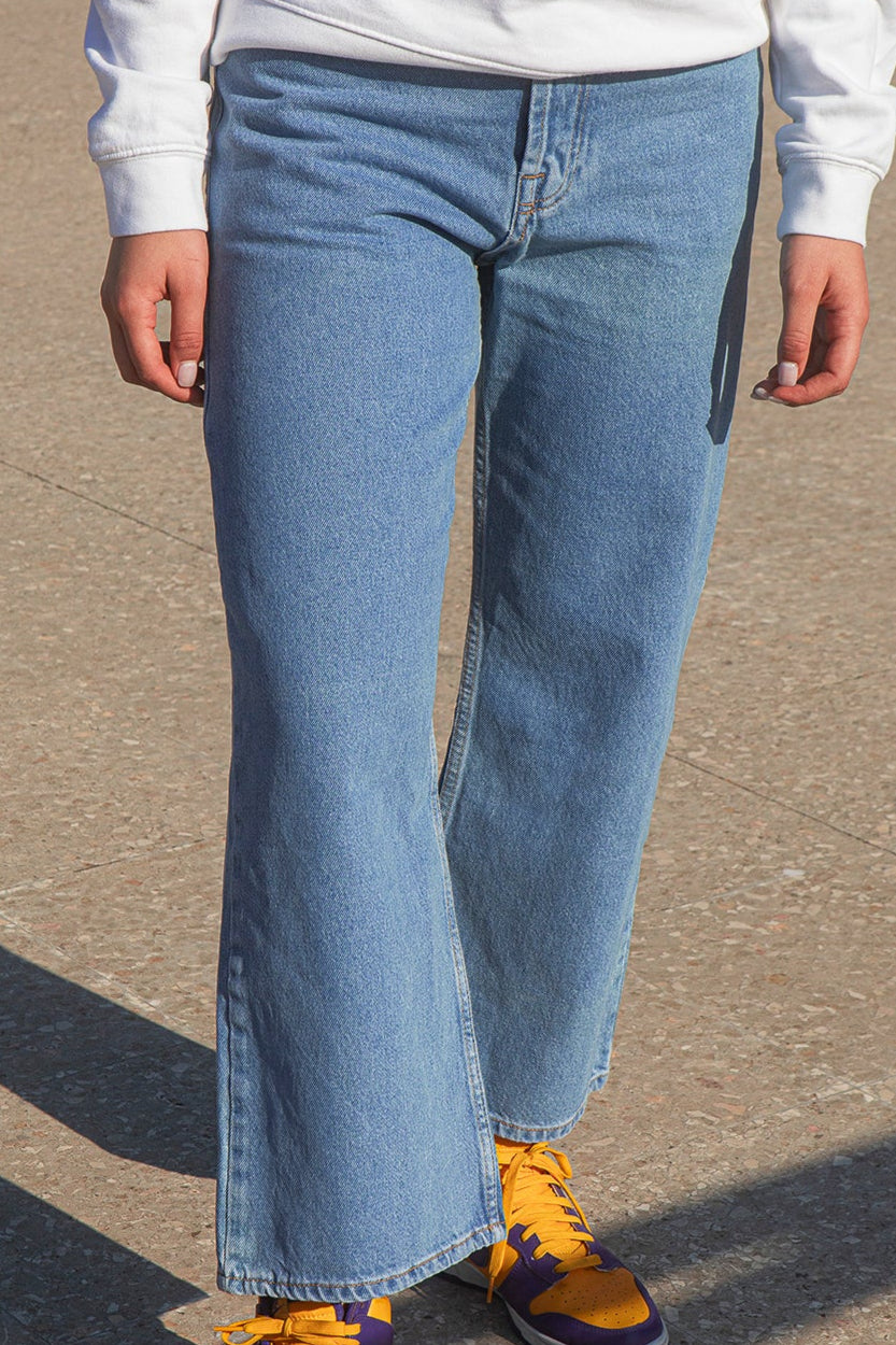 Person wearing blue jeans and yellow sneakers on a concrete surface