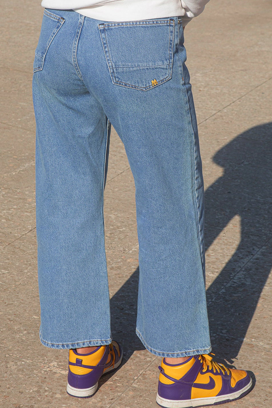 Person wearing blue jeans and yellow sneakers on a concrete surface