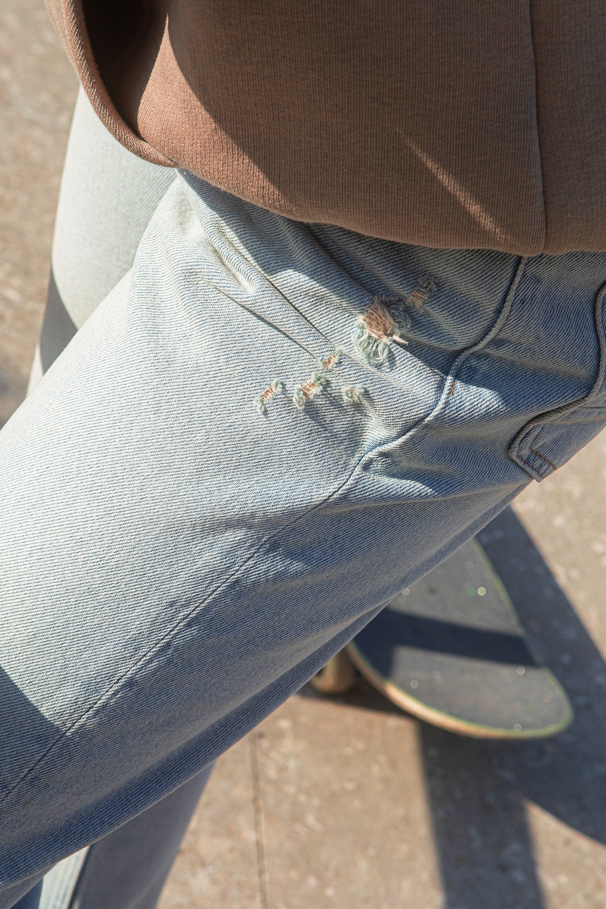Close-up of BENJI premium jeans with a brown shirt and skateboard on a concrete surface