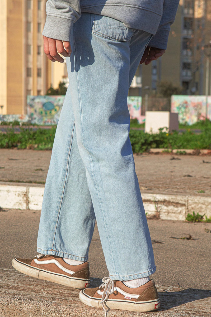 Person wearing light blue jeans and brown shoes standing on a concrete ledge with a blurred urban background.