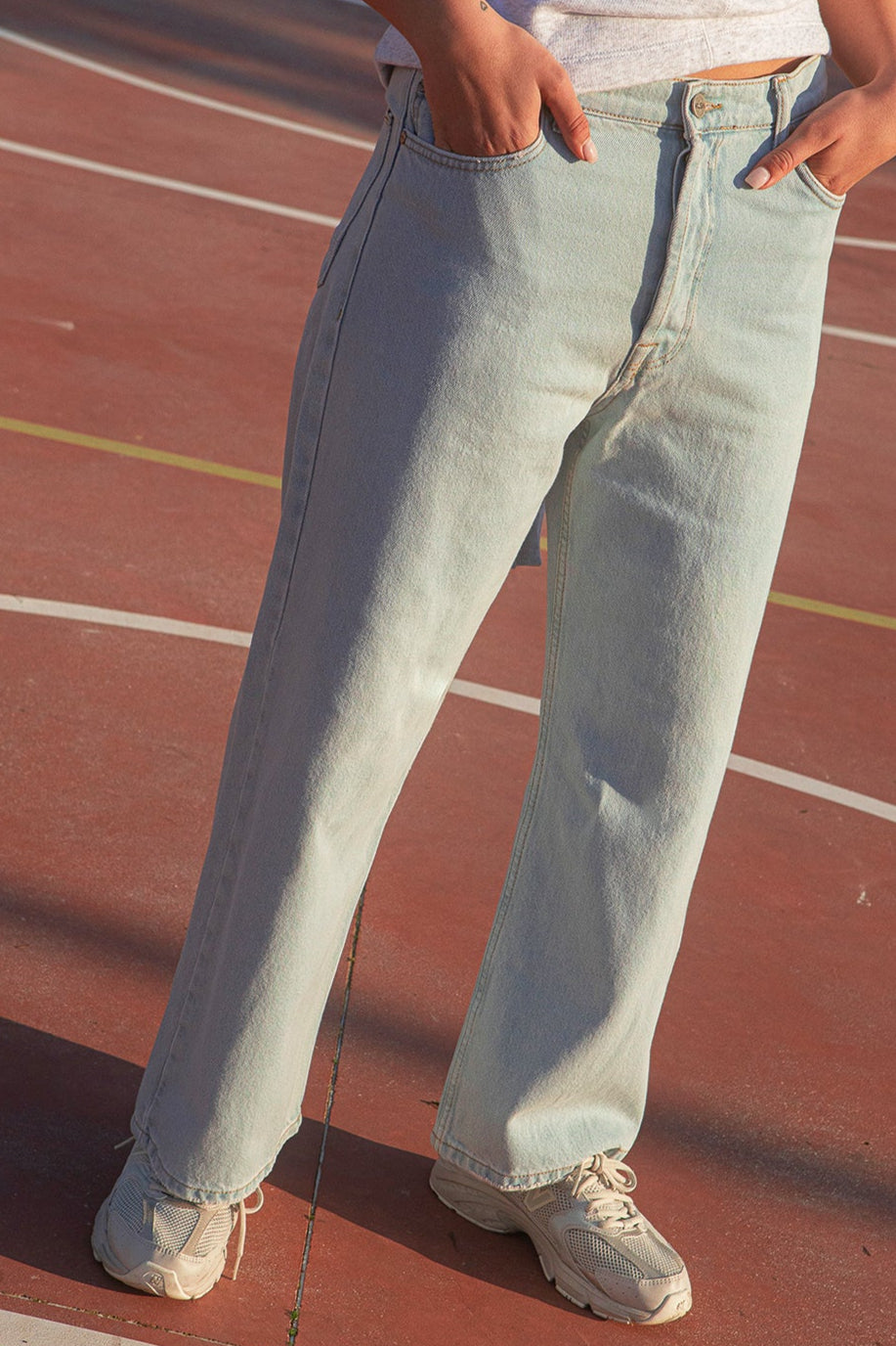 Person wearing the KLSH RYAN clear sky jeans and white sneakers on a red track.