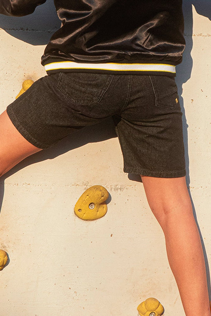 Person on BLAKE Denim shorts climbing on a rock wall with yellow holds