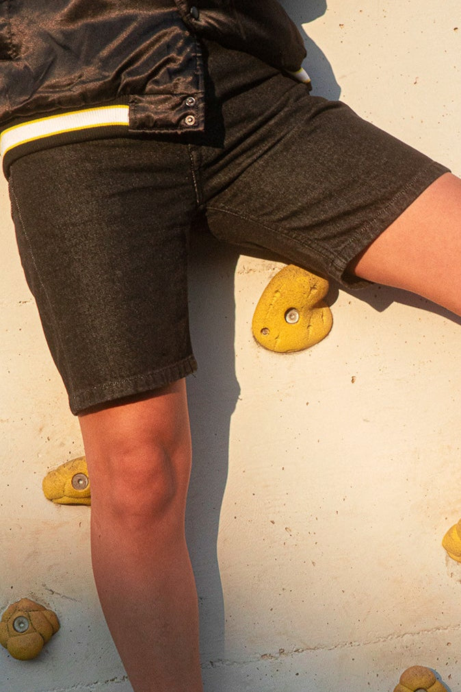 Person on BLAKE Denim shorts climbing on a rock wall with yellow holds