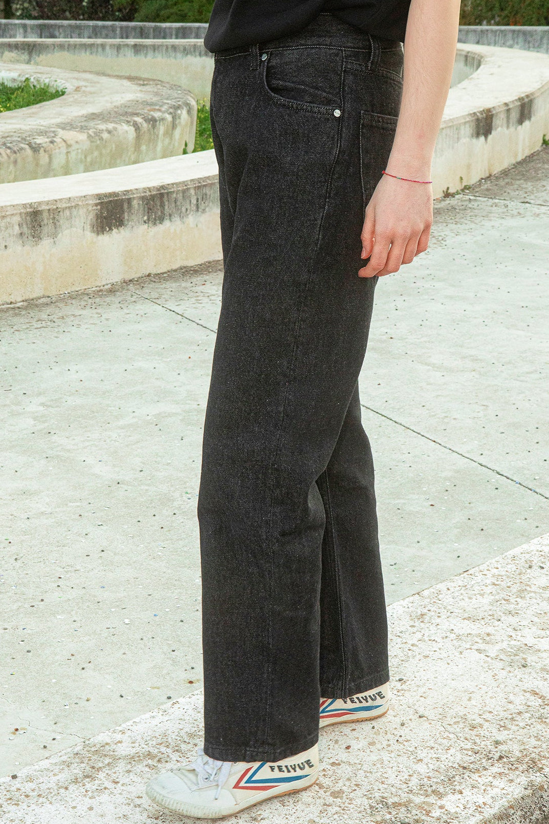 Person wearing black jeans and white sneakers with colorful sole on a concrete surface.