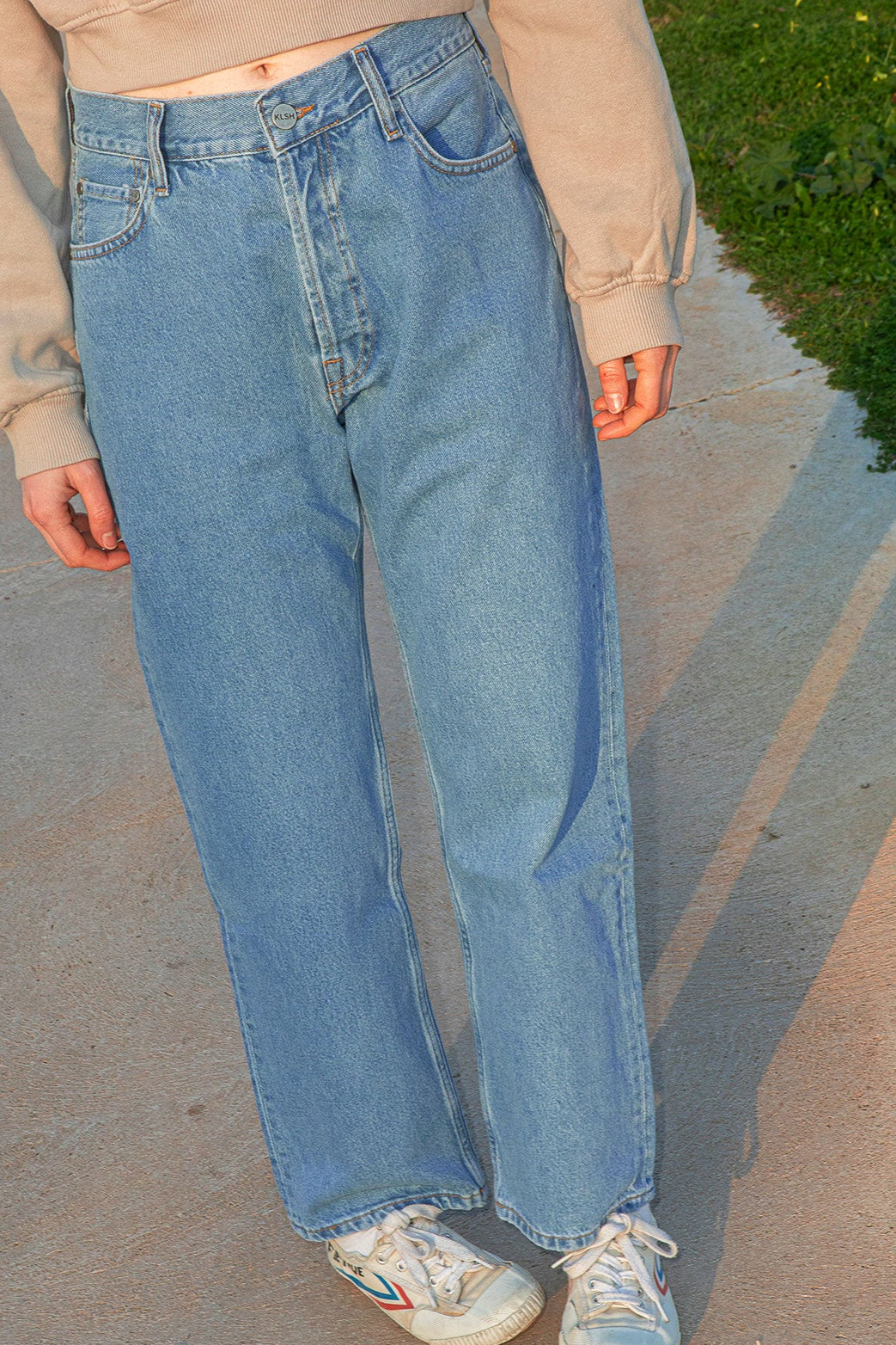 Person wearing light blue jeans and a beige sweatshirt on a concrete surface.