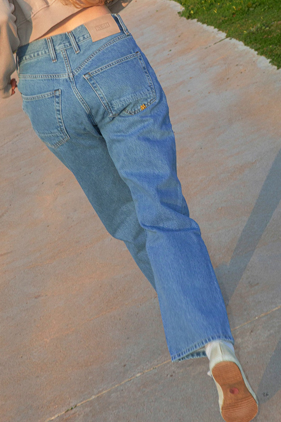 Person wearing light blue jeans and a beige sweatshirt on a concrete surface.