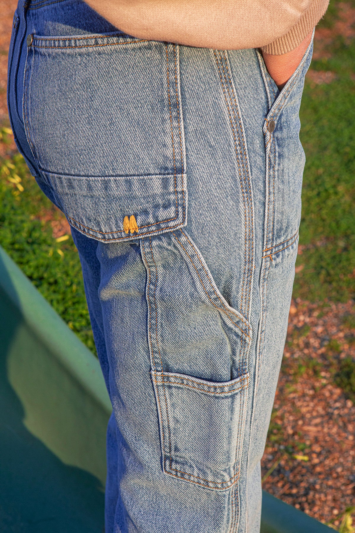 Close-up of faded blue jeans with a brand logo on a grassy background