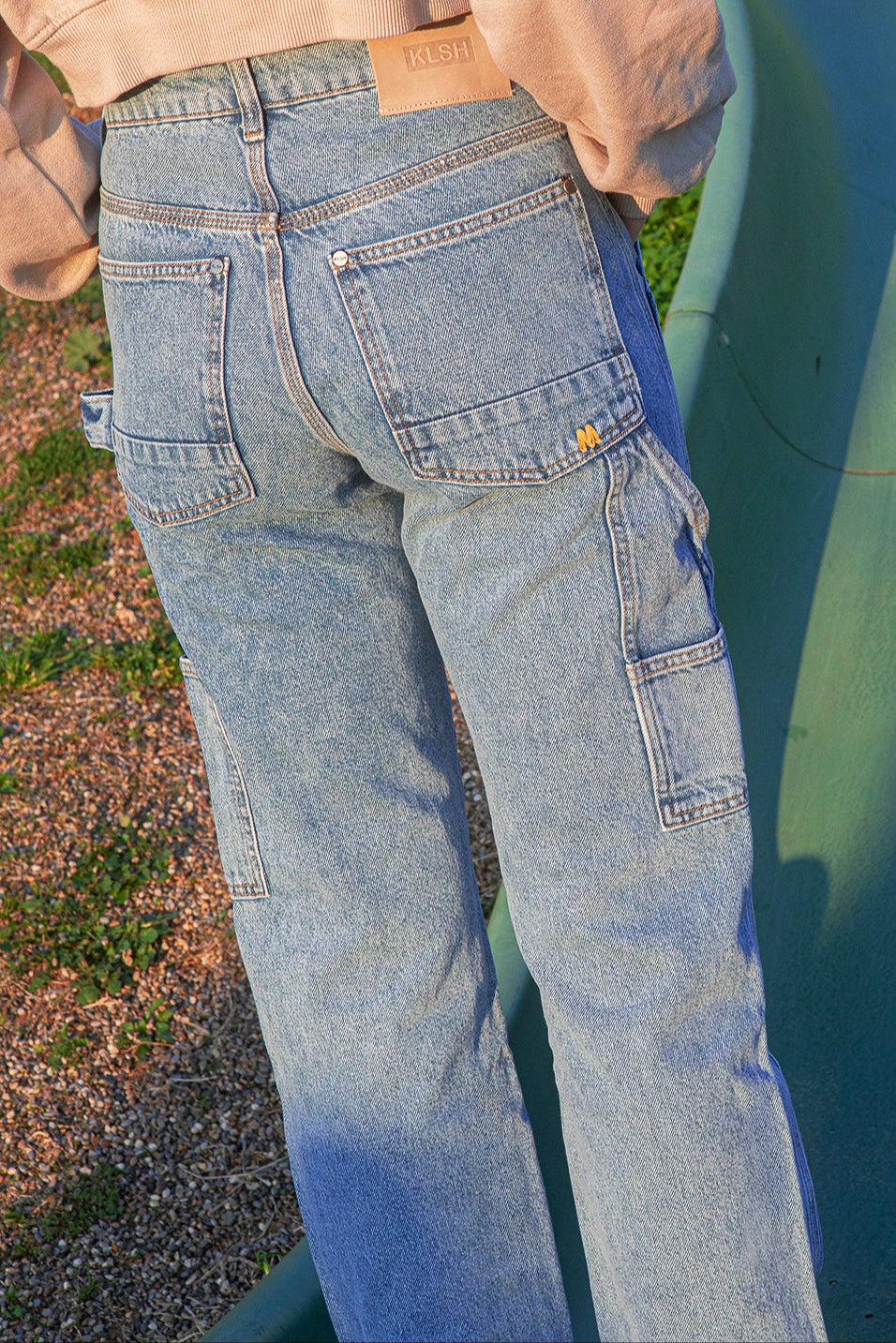 Person wearing faded blue jeans and a beige jacket standing on a green slide.