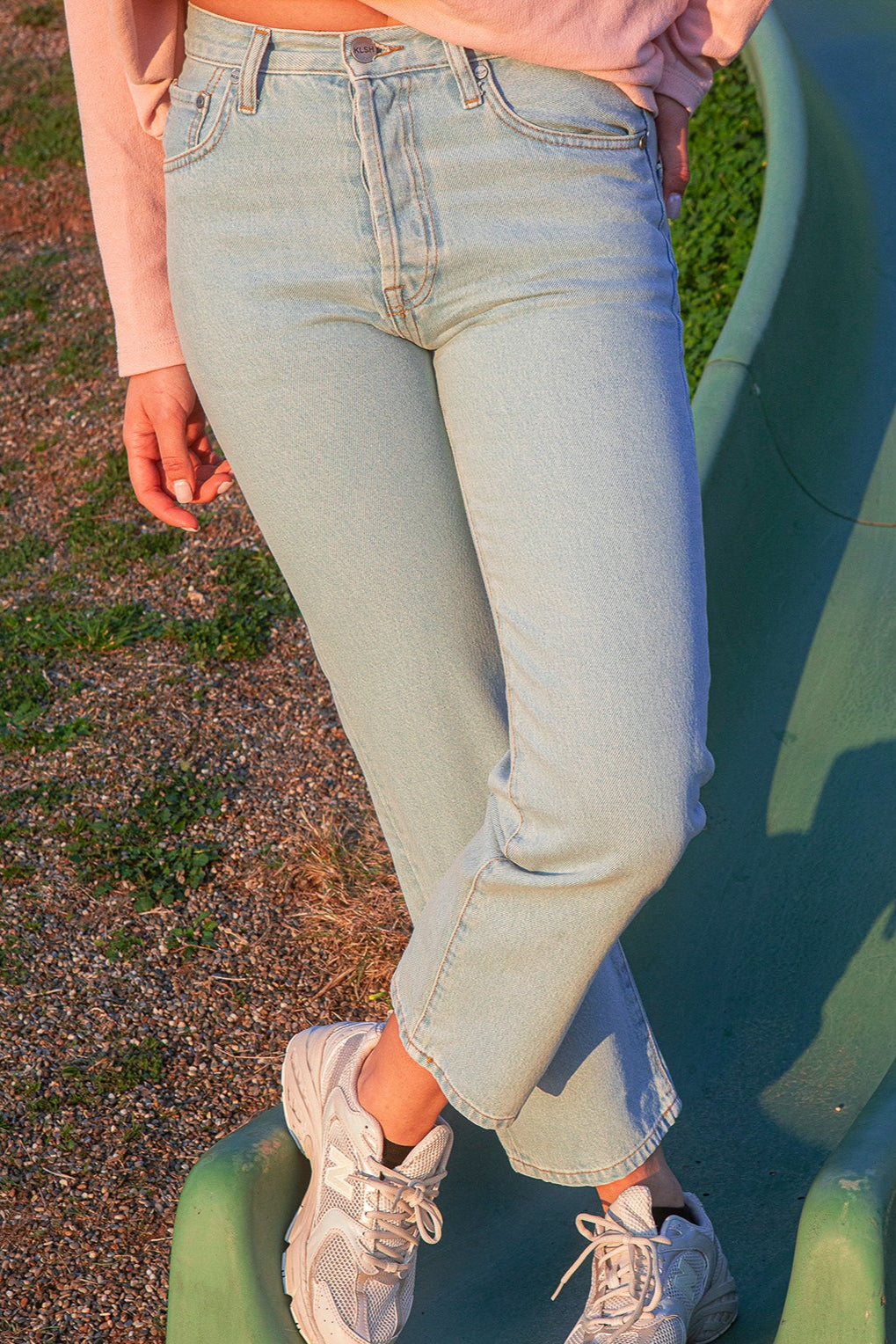 Person wearing the KLSH RYAN clear sky jeans and white sneakers on a red track.