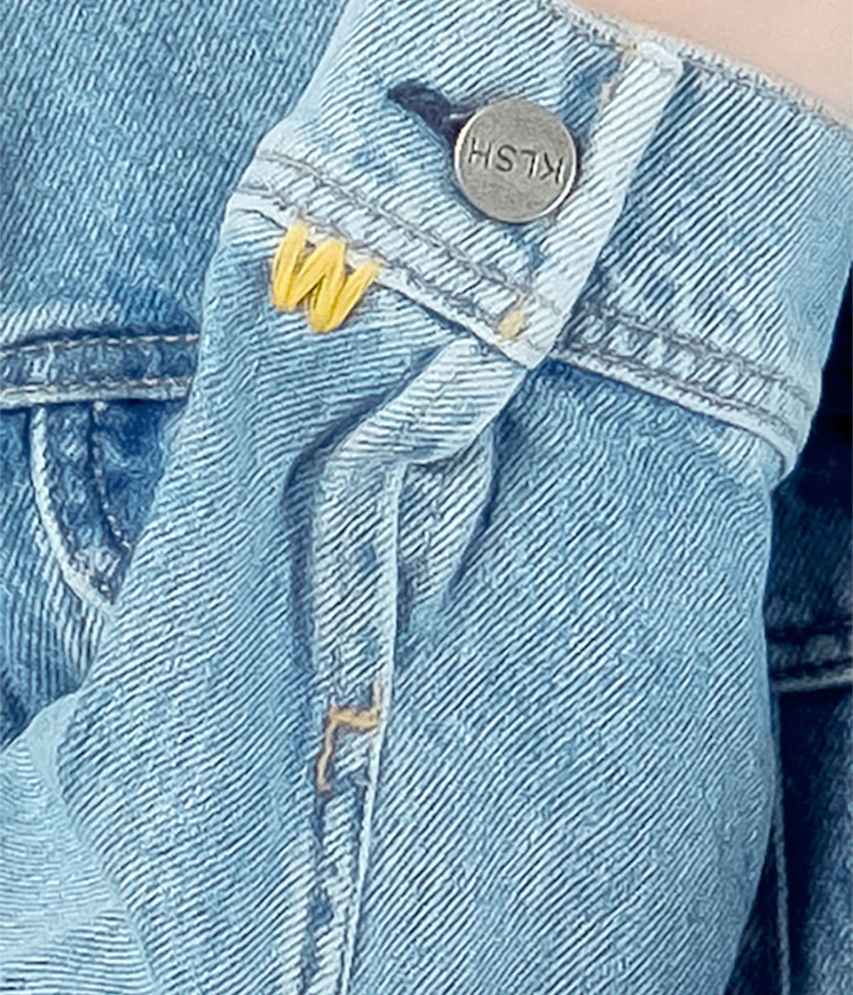 Close-up of a blue denim jacket with a yellow logo and metal button.