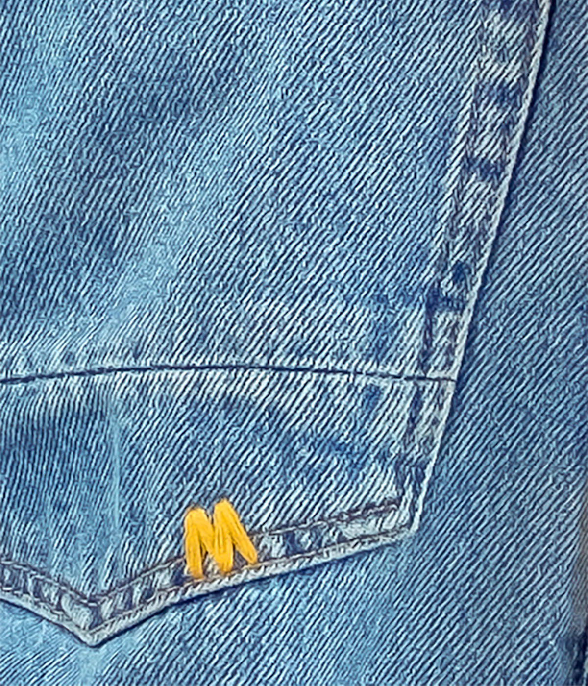 Close-up of a blue denim pocket with a yellow logo on a gray background